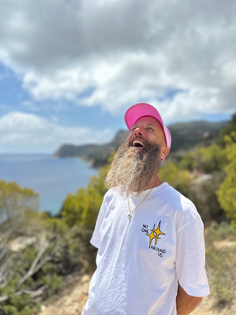 Peter Adams laughing, head thrown back, on the Ibiza coast